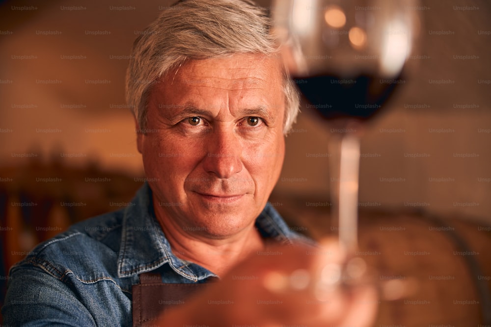 그의 손에 알코올 음료 잔을 보고 있는 남성 와인 메이커의 클로즈업