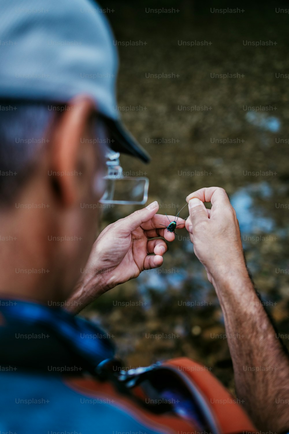 Primo piano delle mani del pescatore anziano che legano una mosca per la pesca. Concetto di pesca a mosca. Vista dall'alto. Vista ad alto angolo sopra la spalla.