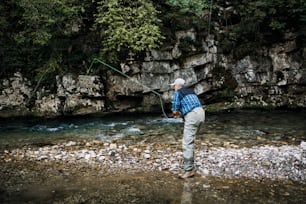 Un homme âgé pêche seul sur une rivière de montagne rapide. Concept de pêche à la mouche active et sportive.