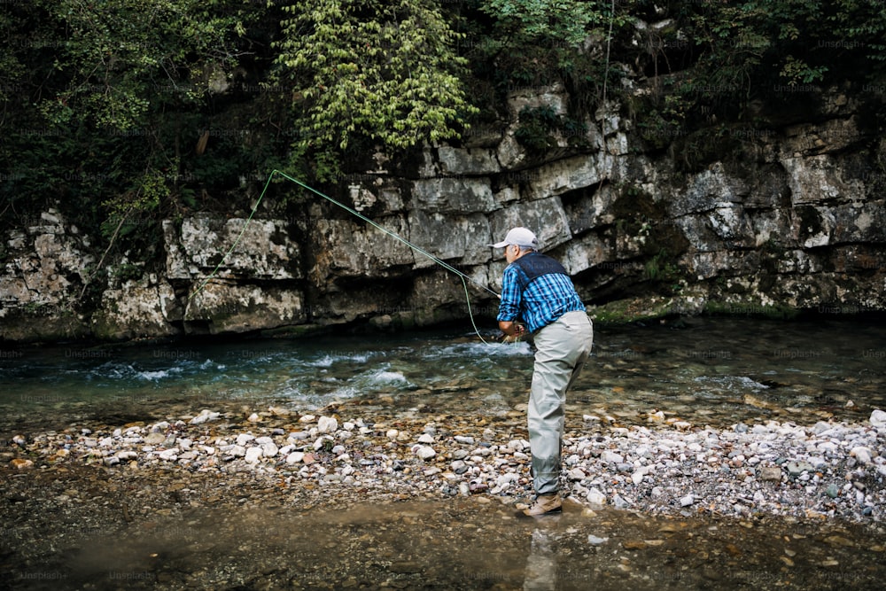 El hombre mayor está pescando solo en un rápido río de montaña. Gente activa y concepto de pesca con mosca deportiva.