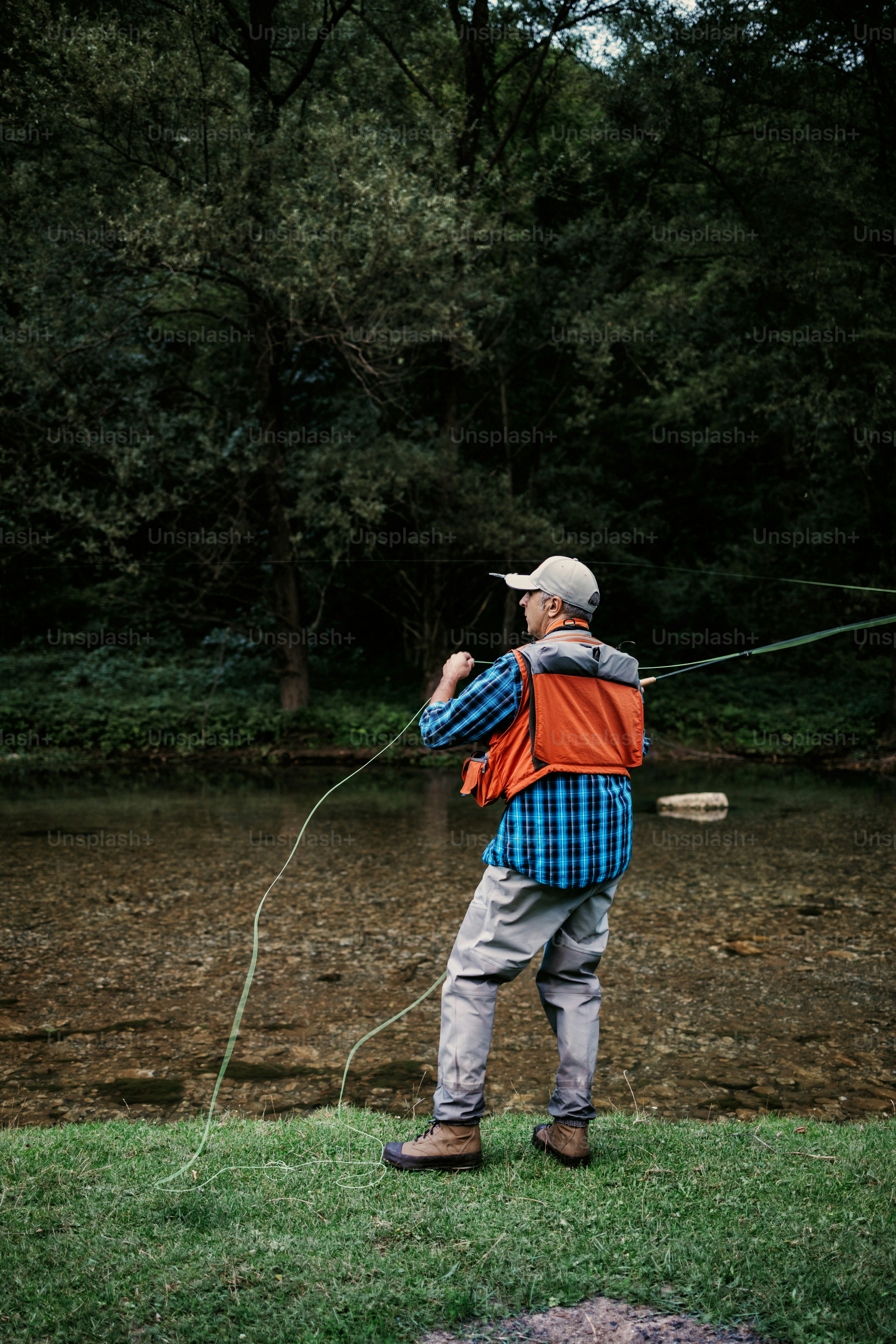 O homem idoso está pescando sozinho no rio da montanha rápida. Pessoas ativas e conceito de pesca com mosca esportiva.