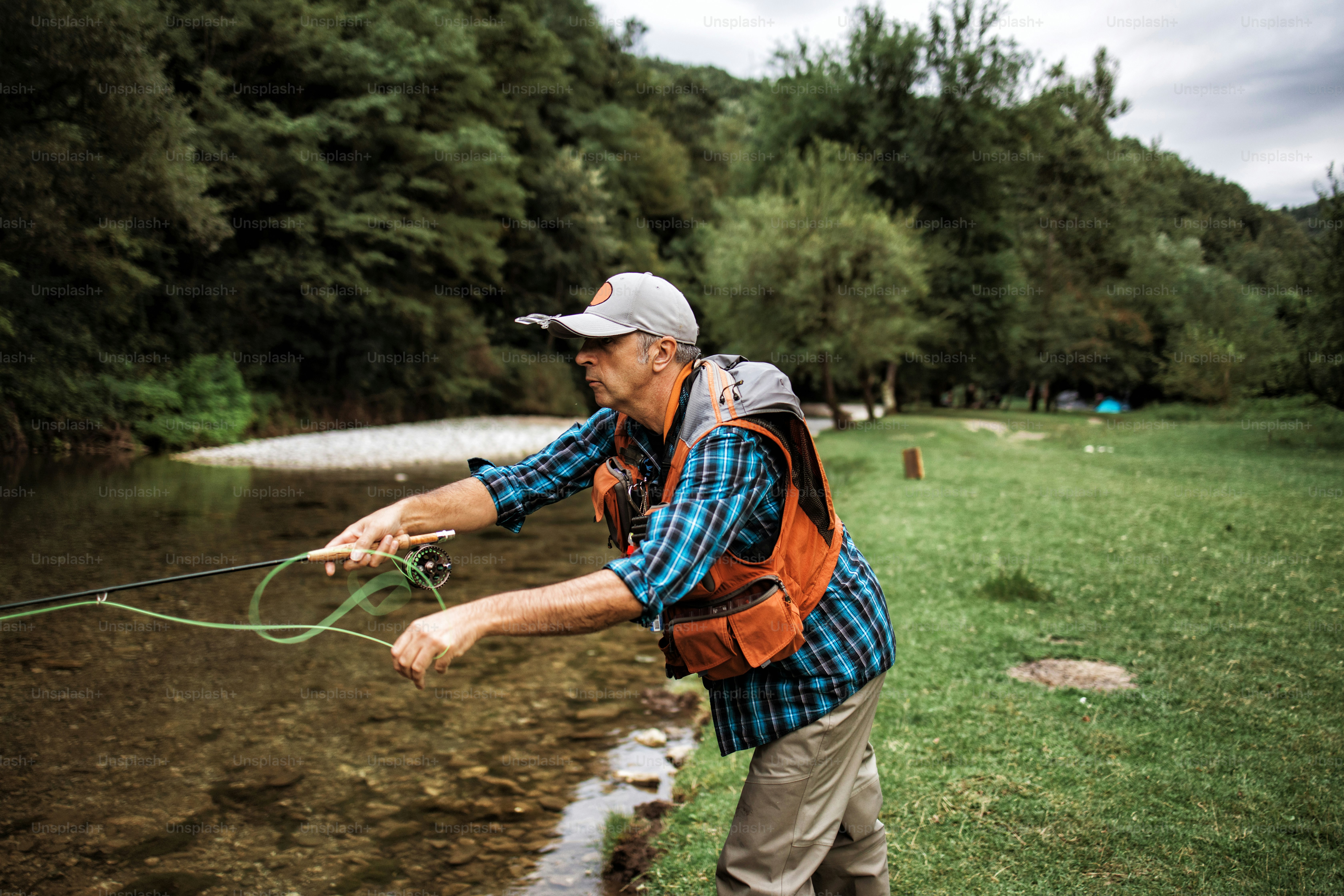 O homem idoso está pescando sozinho no rio da montanha rápida. Pessoas ativas e conceito de pesca com mosca esportiva.