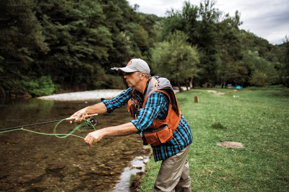 Der ältere Mann fischt alleine auf einem schnellen Gebirgsfluss. Aktive Menschen und Sport-Fliegenfischer-Konzept.