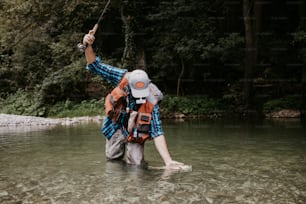 Senior man is fishing alone on fast mountain river. He is holding a live trout and kisses it before releasing it into the river again.