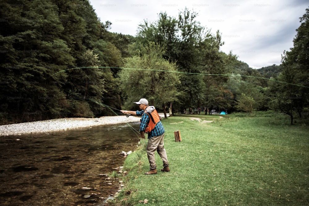 L'uomo anziano sta pescando da solo sul fiume di montagna veloce. Persone attive e concetto di pesca a mosca sportiva.