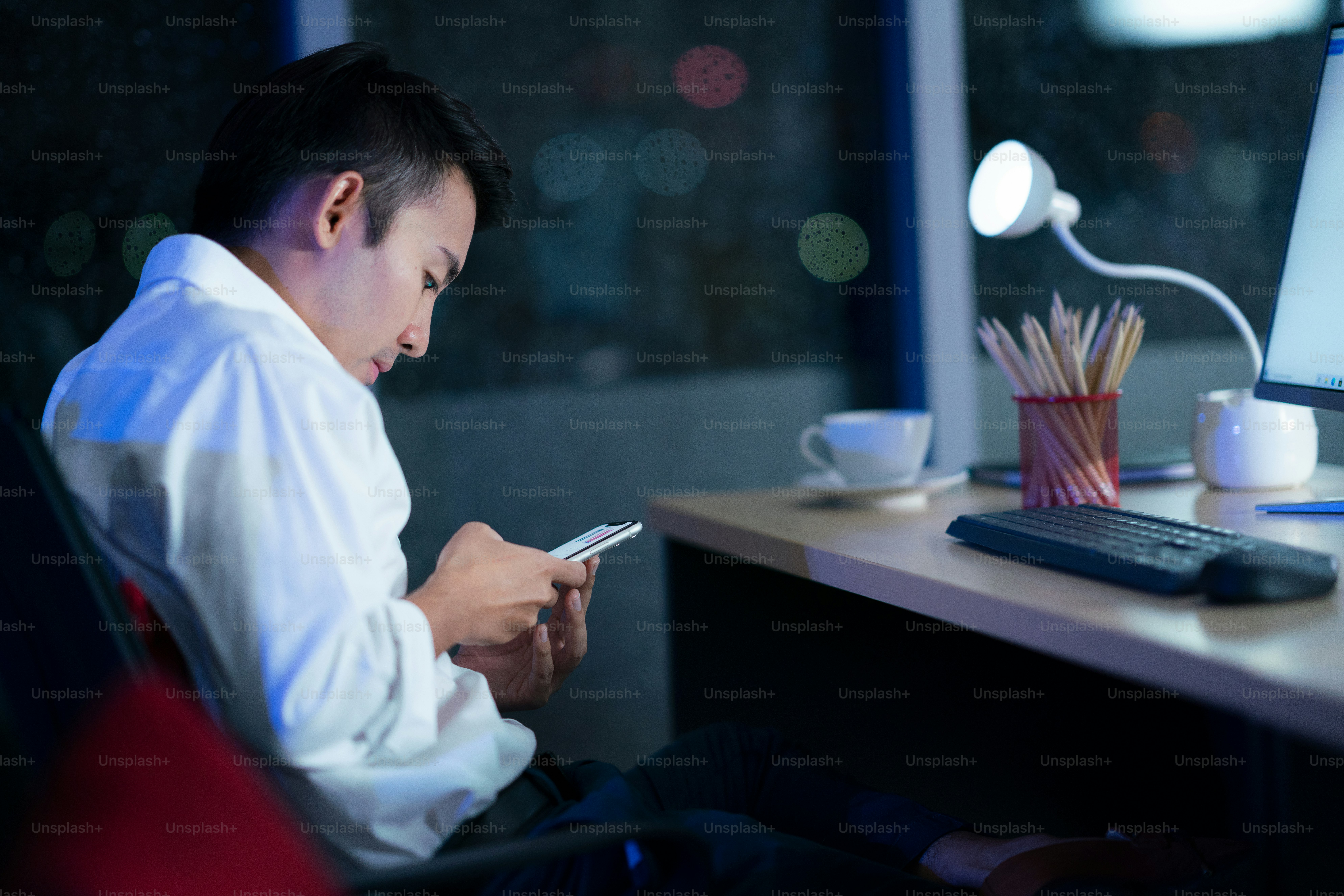 Pekerja kantoran, pekerja pria muda thailand melihat ponsel pintar di kantor larut malam. Konsep kerja malam.