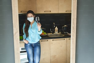 Front view of a woman with a glass of red wine leaning against the countertop
