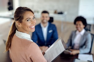 オフィスで仕事に応募し、カメラを見ている幸せな女性。