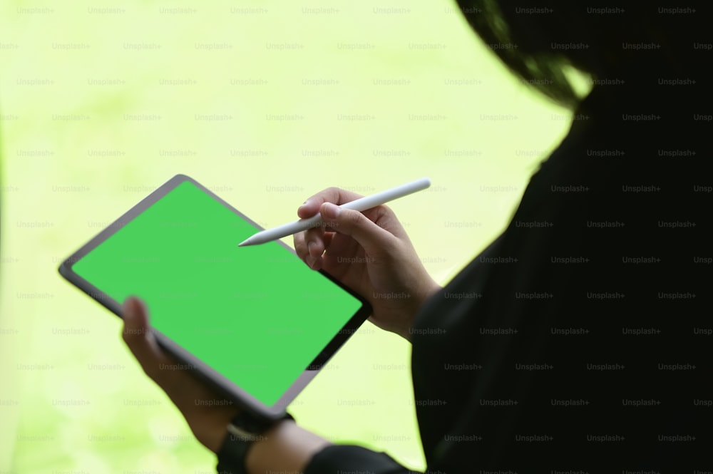 Cropped shot woman using digital tablet and holding stylus pen with green screen device.