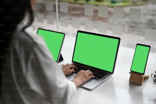 Business woman using computer, taplet, smartphone with green screen and looking at screen working in internet and sit at office desk.