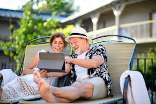 Portrait of senior couple with tablet outdoors on holiday, relaxing.