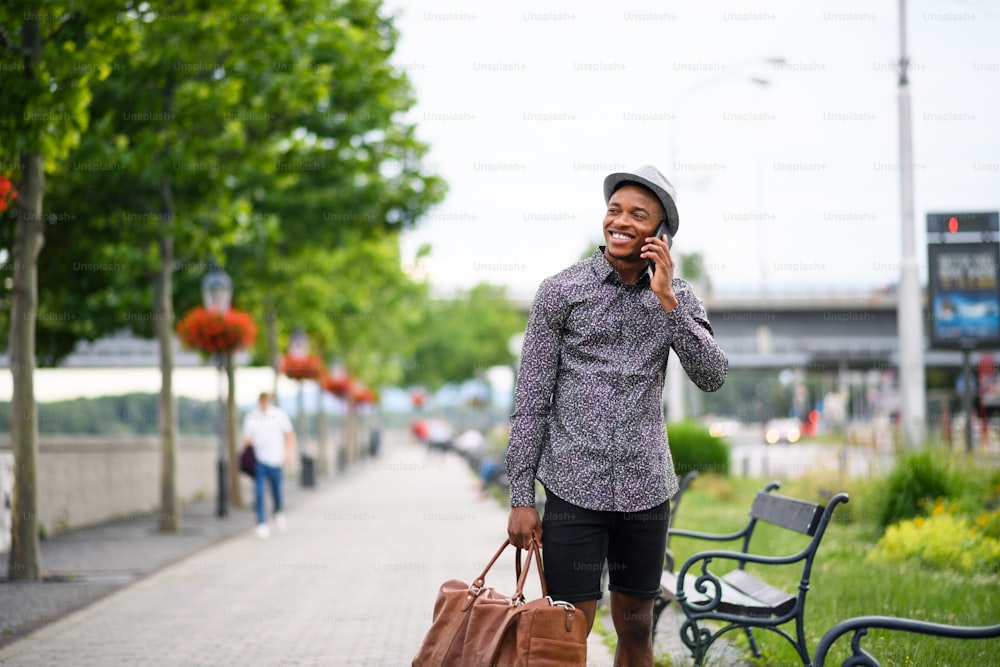 Front view of cheerful young black man commuter outdoors in city, using smartphone.