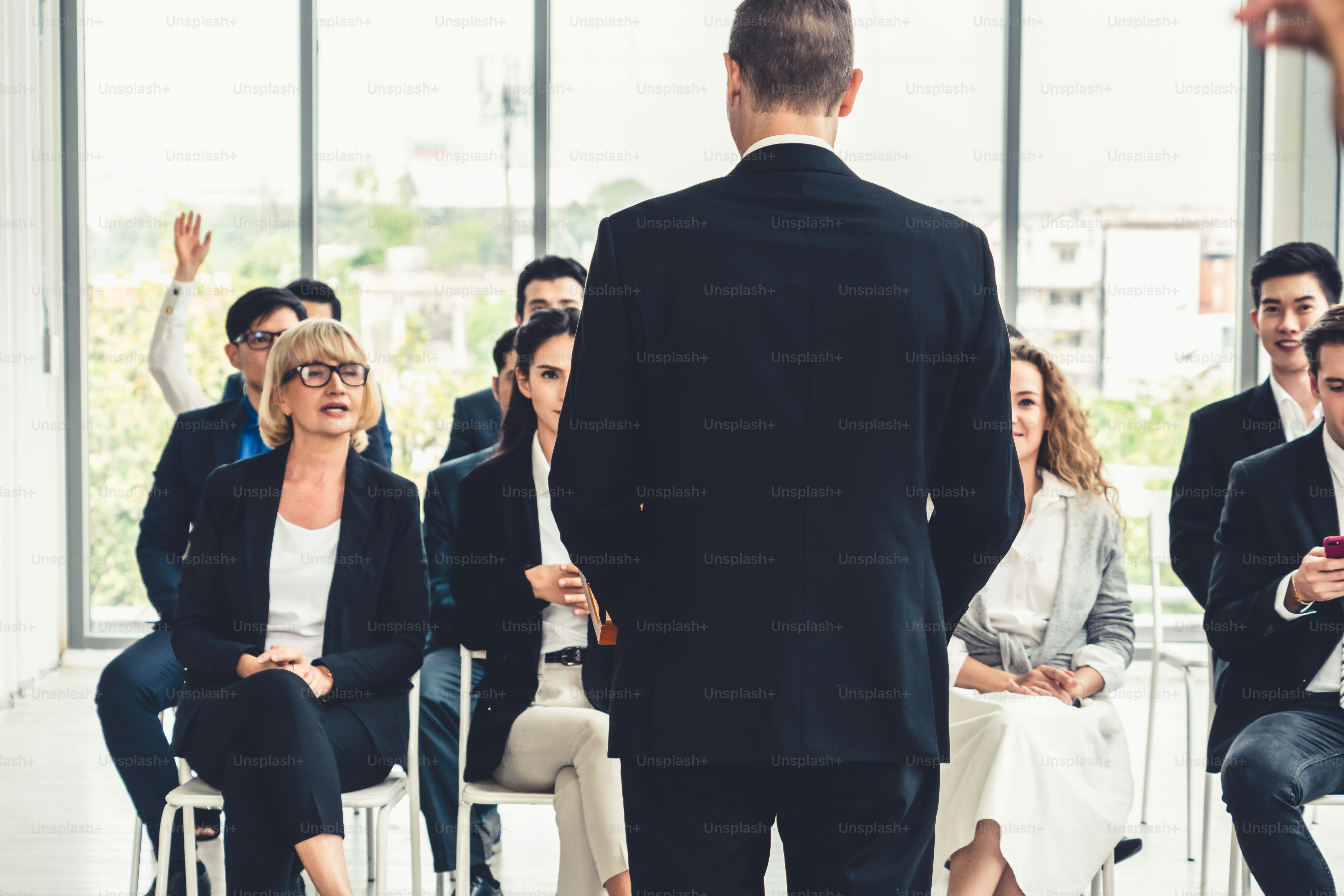 Una persona in giacca e bassa che presenta a un gruppo di persone in una sala conferenze