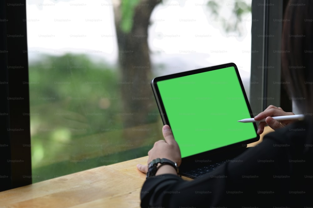 デジタルタブレットのグリーンスクリーンでスタイラスペンを使用する女性の接写。