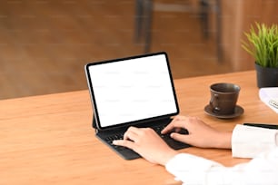 Foto recortada de una mujer usando una tableta negra con pantalla blanca sobre una mesa de madera.