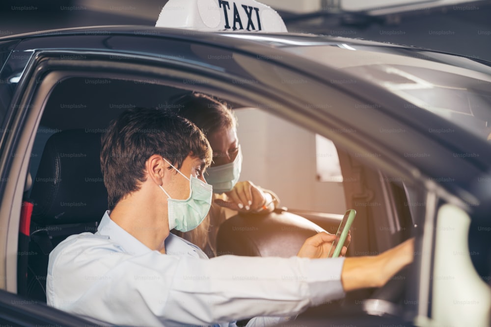 Neue Normalität. Teenager sitzt auf dem Rücksitz eines Autos mit einer Maske. Junge Frau in einem Taxi, geschützt durch eine Maske. Verkehrssicherheit. Coronavirus-Pandemie. Smartphone verwenden Route suchen