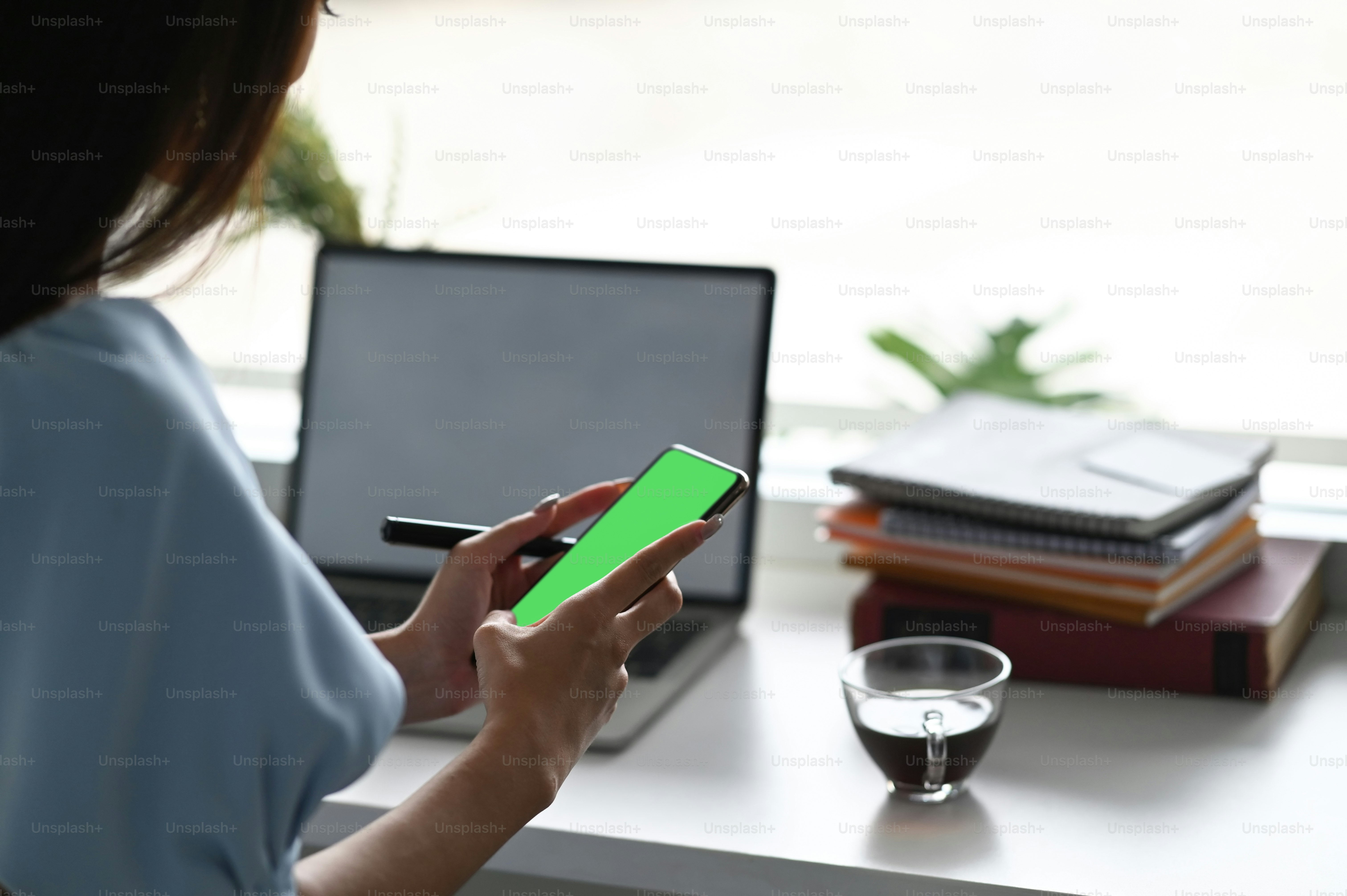 Mujer de primer plano mirando su teléfono inteligente y chateando con sus amigos en el interior. Hay una computadora portátil en la mesa frente a ella.