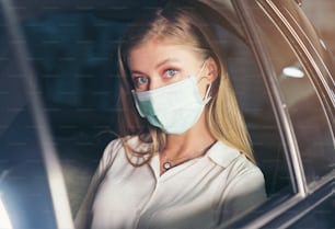 Neue Normalität. Teenager sitzt auf dem Rücksitz eines Autos mit einer Maske. Junge Frau in einem Taxi, geschützt durch eine Maske. Verkehrssicherheit. Coronavirus-Pandemie.