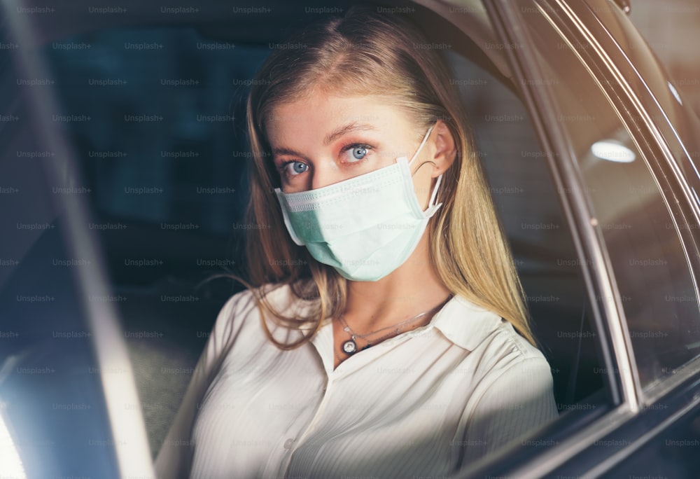 新しい標準。マスクをして車の後部座席に座っているティーンエイジャー。マスクで守られたタクシーの若い女性。交通安全。コロナウイルスパンデミック。