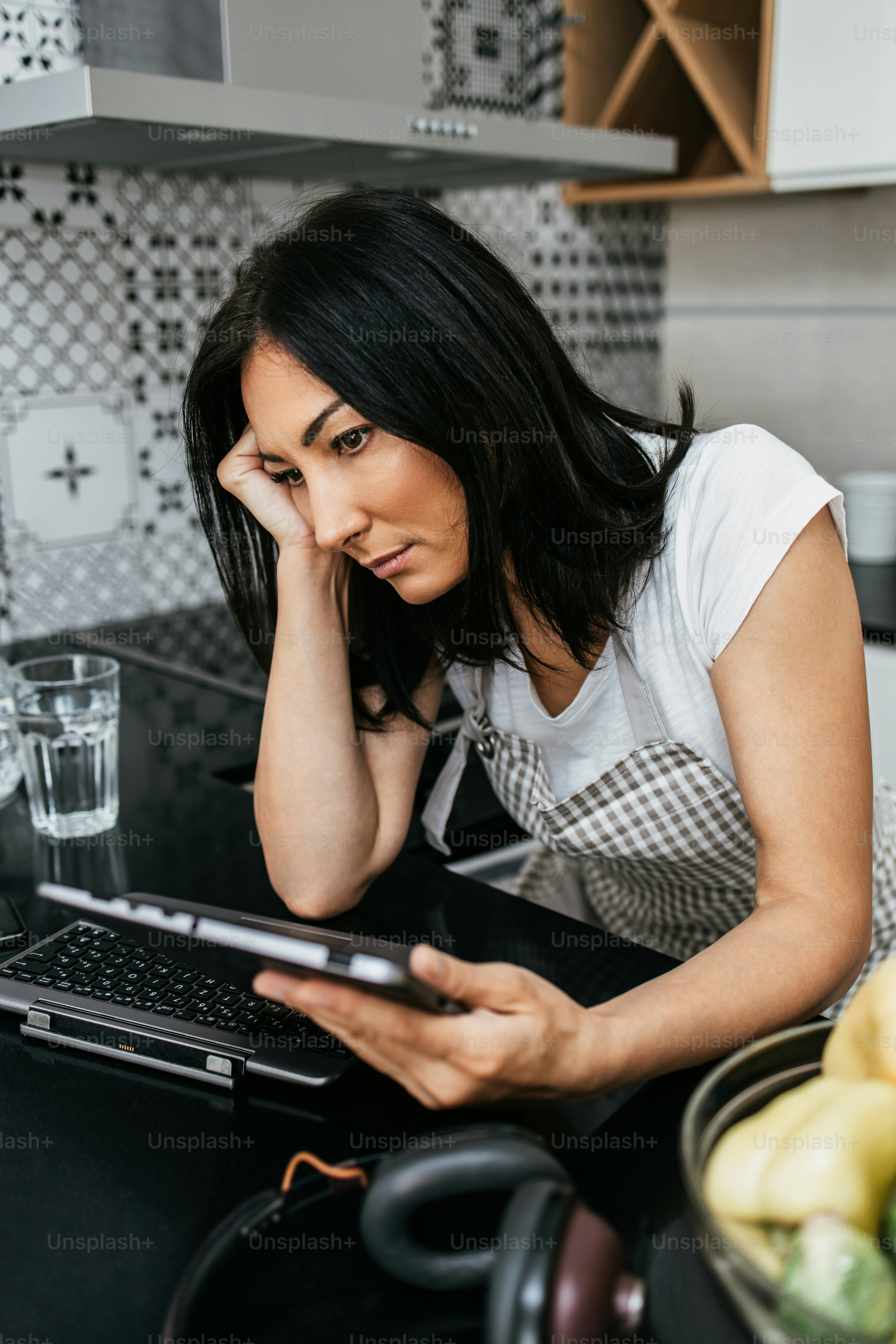 Beautiful and worried middle age woman sitting alone in her apartment. She gets bored but tries to stay positive. She uses laptop computer and tablet to chat and listen to music.