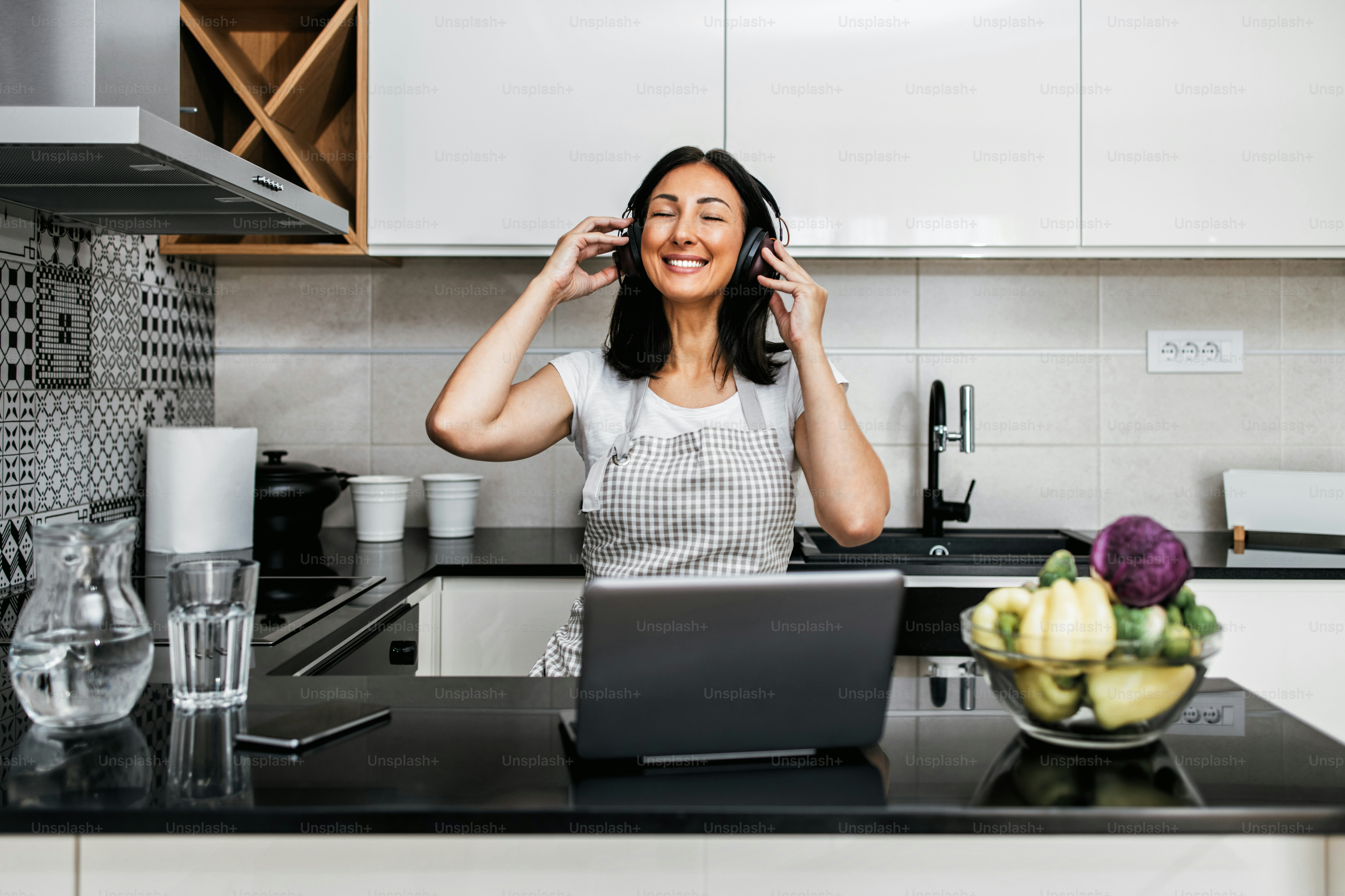 Beautiful middle age woman sitting alone in her apartment. She gets bored but tries to have a good time and stay positive. She uses laptop computer and tablet to chat and listen to music.