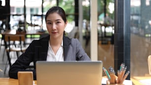 Portrait of businesswoman in suit looking into camera while working with laptop in cafe