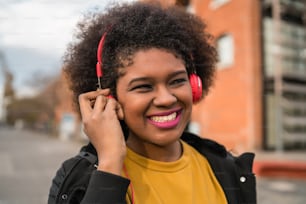 Portrait of afro american woman smiling and listening to music with headphones in the street. Outdoors.