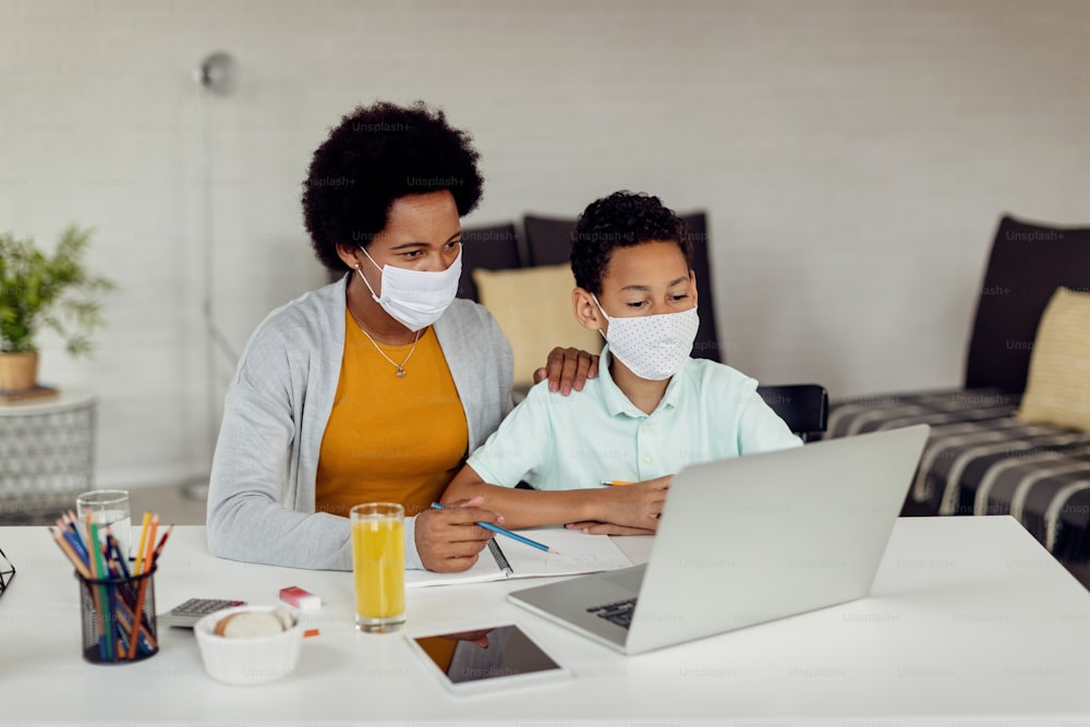African American homeschooling mother and her son using computer while e-learning during COVID-19 pandemic.