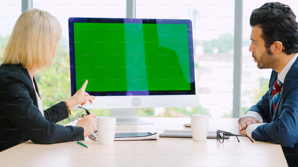 Des gens d’affaires dans la salle de conférence avec écran vert, une télévision à clé chromatique ou un ordinateur sur la table du bureau. Groupe diversifié d’hommes et de femmes d’affaires en réunion par vidéoconférence.