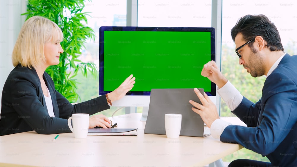 사무실 테이블에 녹색 스크린 크로마 키 TV 또는 컴퓨터가 있는 회의실의 비즈니스 사람들. 화상 회의에서 만나는 사업가와 사업가의 다양한 그룹.
