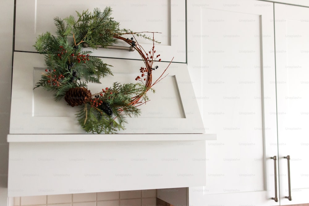 Ghirlanda di Natale moderna creativa appesa su eleganti mobili da cucina. Ghirlanda di Natale rustica appesa alla cappa da cucina moderna, decorazione festiva per le vacanze. Buon Natale e Buone Feste