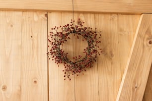 Rustic simple christmas wreath on wooden door indoors, festive holiday decoration. Creative natural christmas wreath made of red berries, hanging on stylish rural door. Merry Christmas