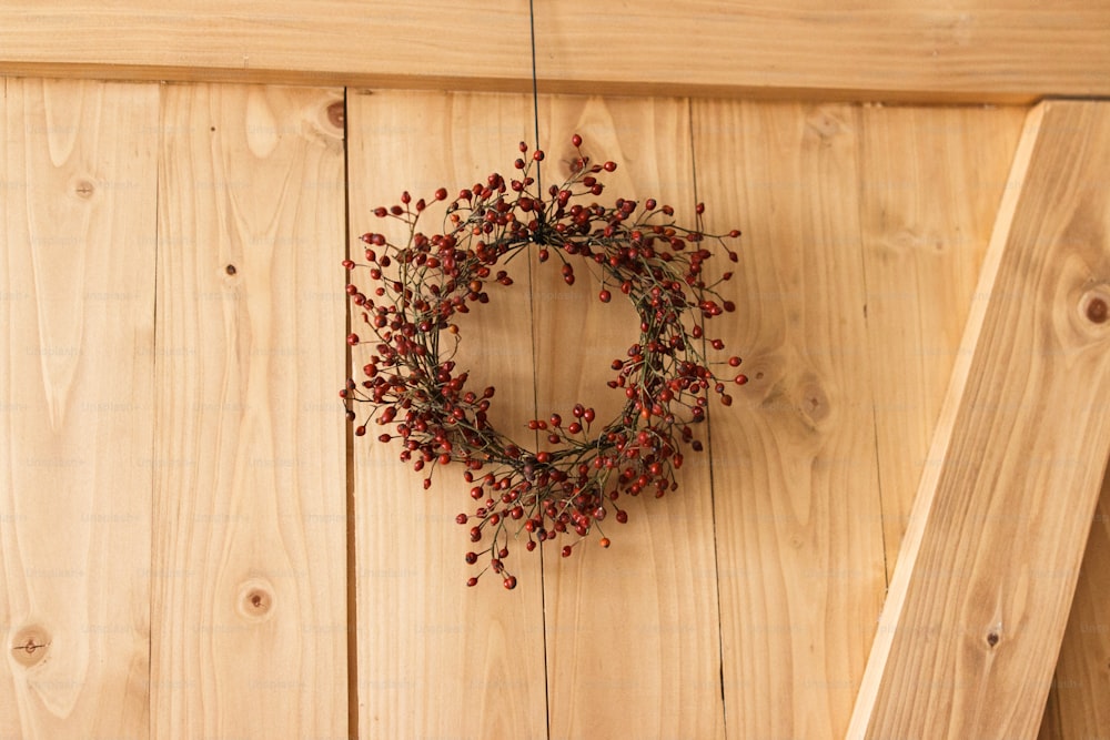 Rustic simple christmas wreath on wooden door indoors, festive holiday decoration. Creative natural christmas wreath made of red berries, hanging on stylish rural door. Merry Christmas