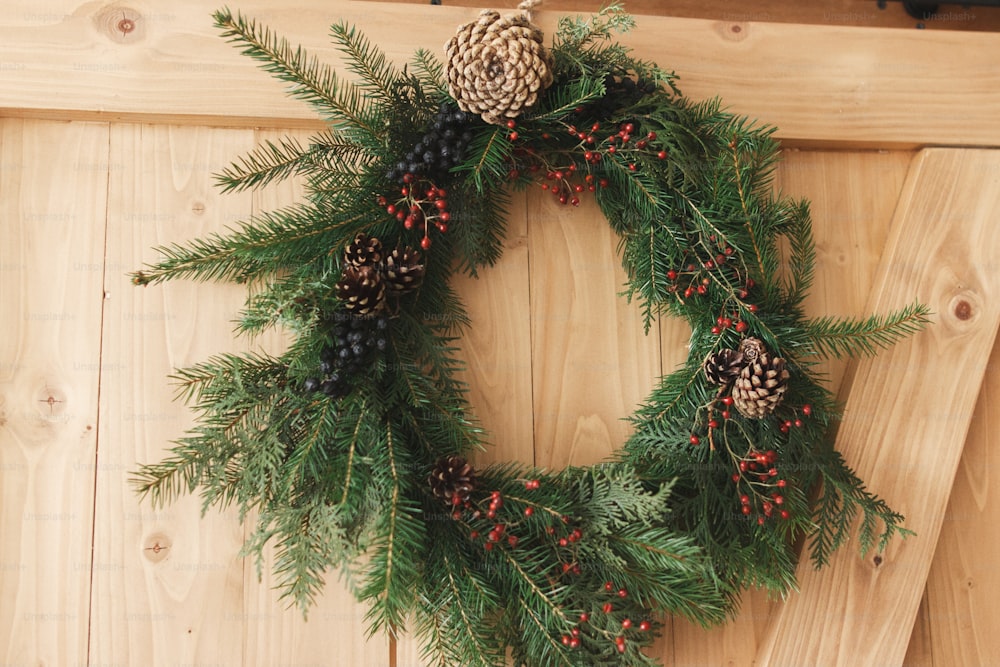 Rustic christmas wreath on wooden door indoors, festive holiday decoration. Creative natural christmas wreath hanging on stylish rural door. Merry Christmas