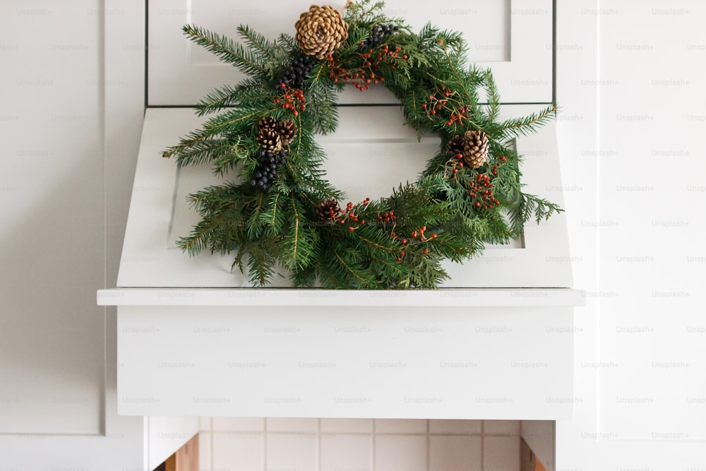 Creative modern christmas wreath hanging on stylish kitchen cabinets. Rustic christmas wreath hanging on modern kitchen hood, festive holiday decoration. Merry Christmas and Happy Holidays