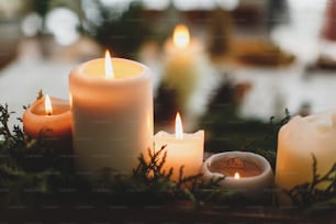 Burning candles on rustic background with christmas wreath, pine cones and ornaments on wooden table in evening. Holiday workshop advent, cozy atmosphere. Copy space