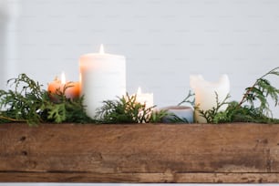 Burning candles in rustic wooden box with cedar branches on wooden table on white background. Festive christmas table decoration, winter holiday decor and wedding arrangement. Copy space