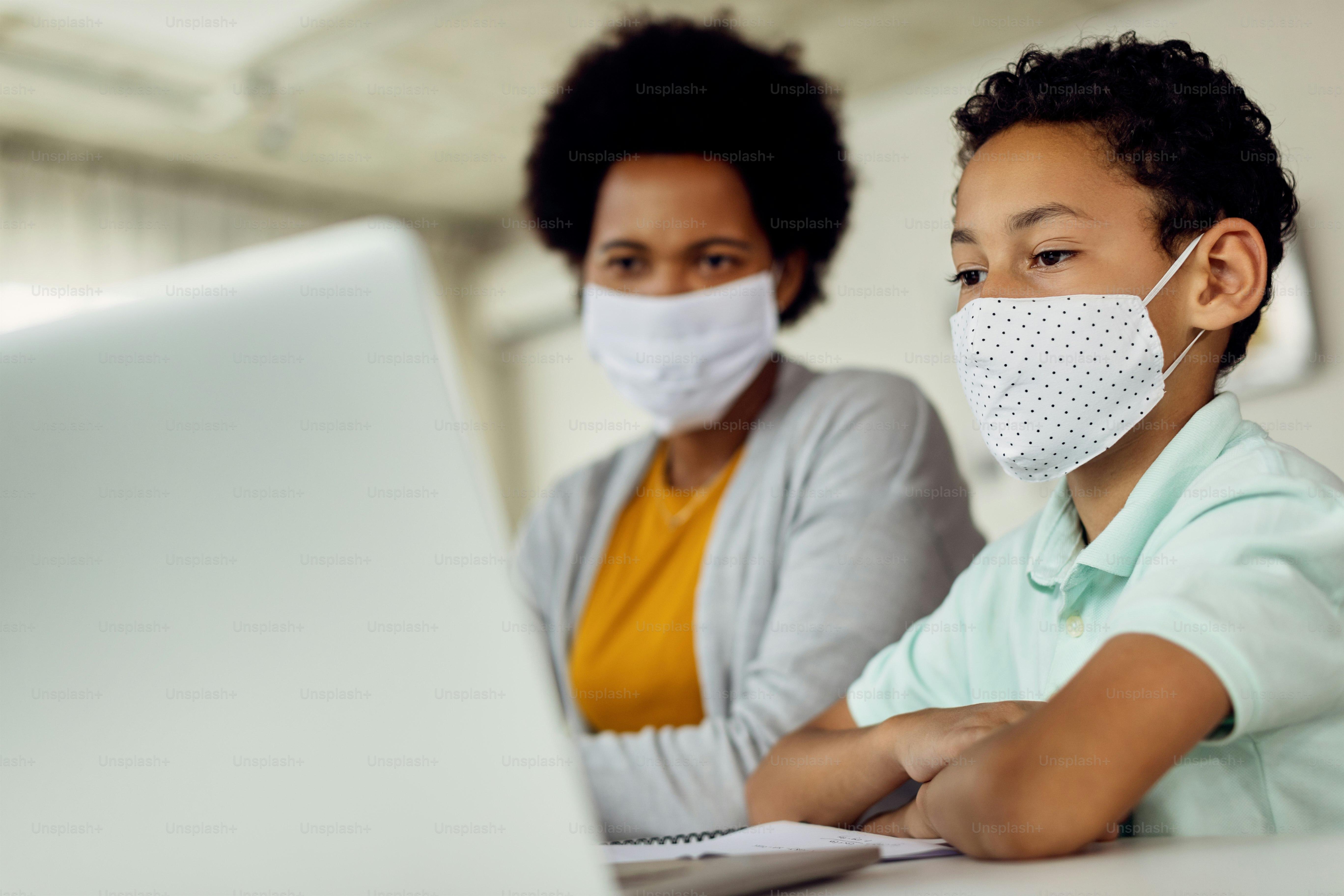 Small black boy using laptop while homeschooling with his mother during coronavirus epidemic.