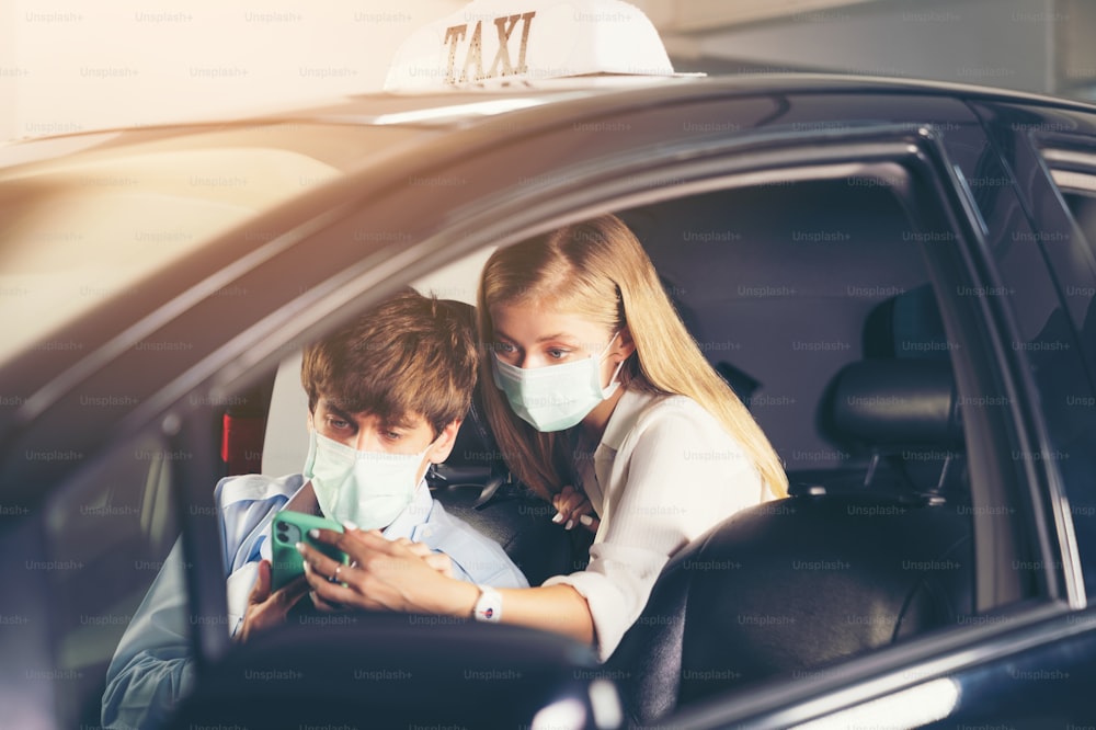 新しい標準。マスクをして車の後部座席に座っているティーンエイジャー。マスクで守られたタクシーの若い女性。交通安全。コロナウイルスパンデミック。スマートフォンのルート検索を使用する