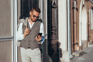 Foto de um belo empresário em um terno andando pela cidade durante o dia e usando um smartphone
