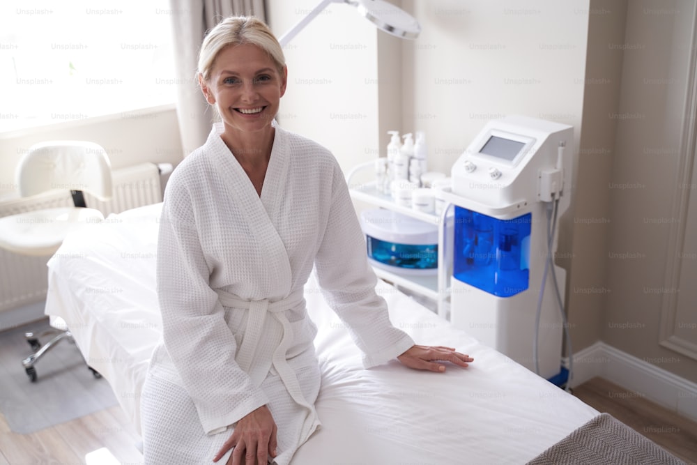 Lächelnde attraktive erwachsene Frau sitzt auf einer Massageliege in einem Massagesalon in der Schönheitsklinik
