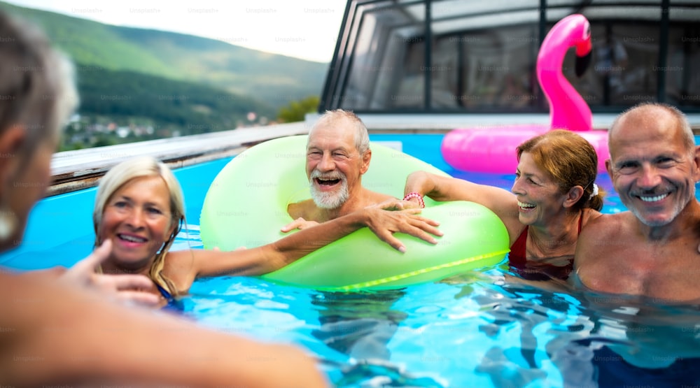 Grupo de idosos alegres na piscina ao ar livre no quintal, conversando e se divertindo.