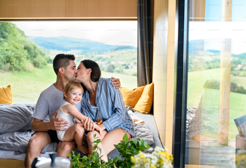 Young family with small daughter kissing indoors, weekend away in container house in countryside.