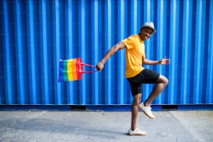 Side view of young black man with rainbow bag walking.