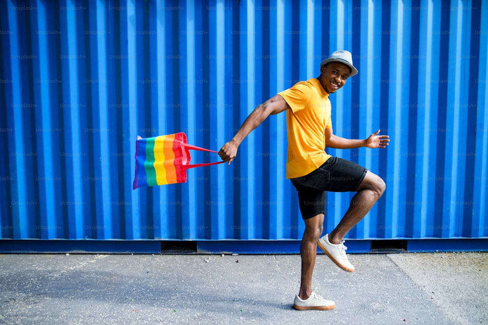Side view of young black man with rainbow bag walking.