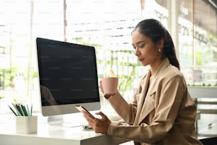 Portrait of young businesswoman looking at her smartphone while drinking coffee in the morning.