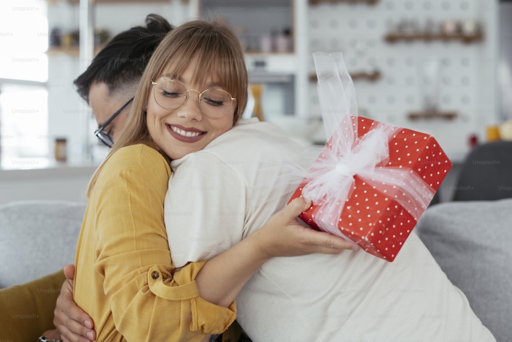 Husband surprising his wife with a gift. Young man giving a gift box to his wife.