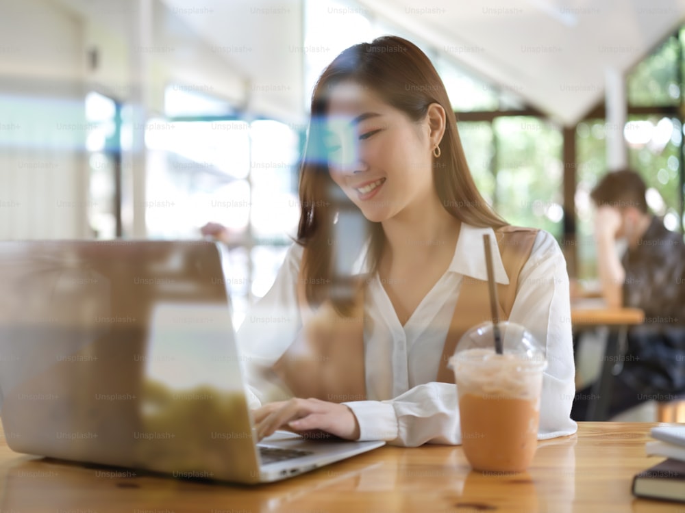 View through glass wall of female college student doing homework with laptop in cafe