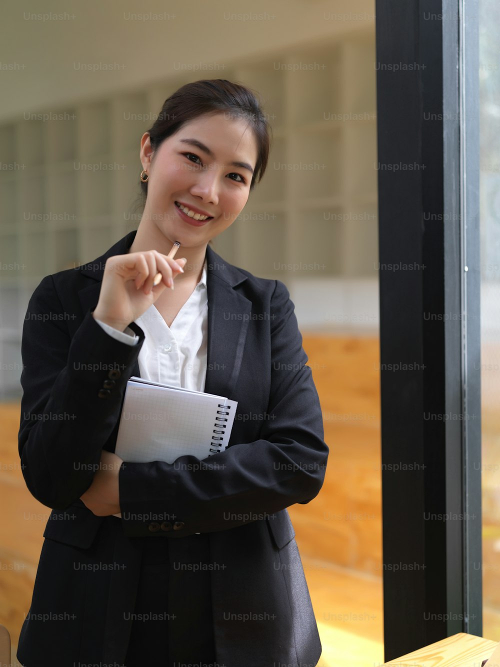 Portrait of female in suit holding schedule book and pen looking into camera and smiling in office room