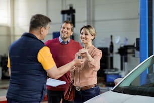 ワークショップで自動車修理工に車のキーを渡す幸せなカップル。